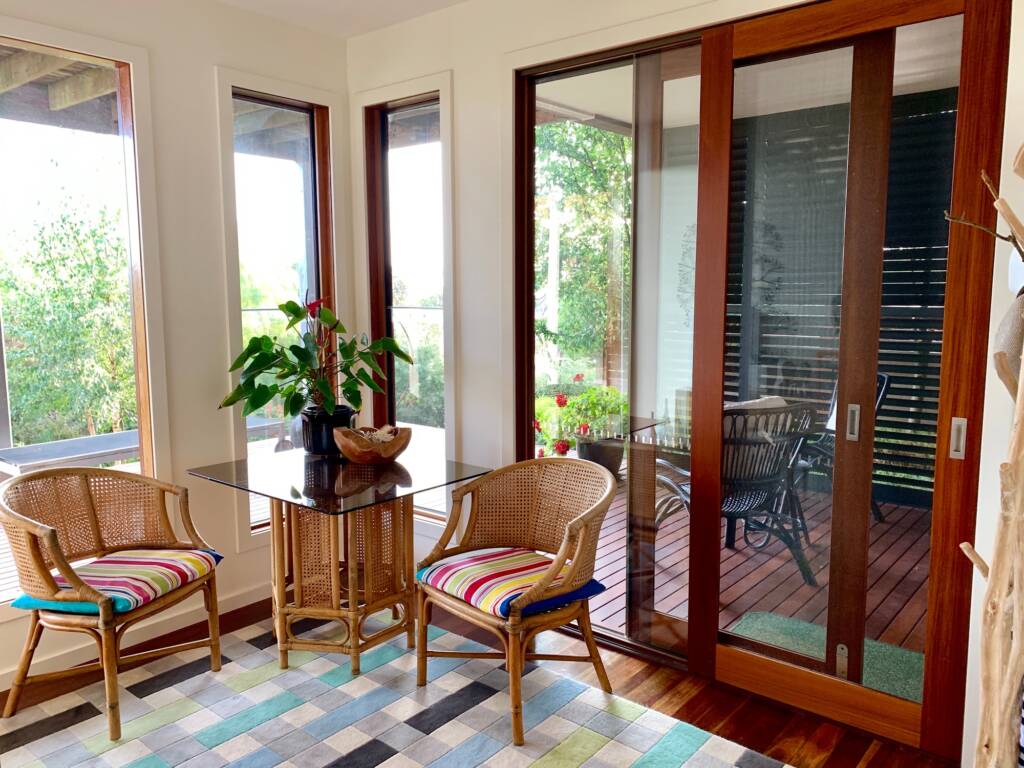 Elegante sala de estar con muebles de ratán, numerosas ventanas y puertas corredizas de caoba - Puertas y ventanas de pvc Termprotect