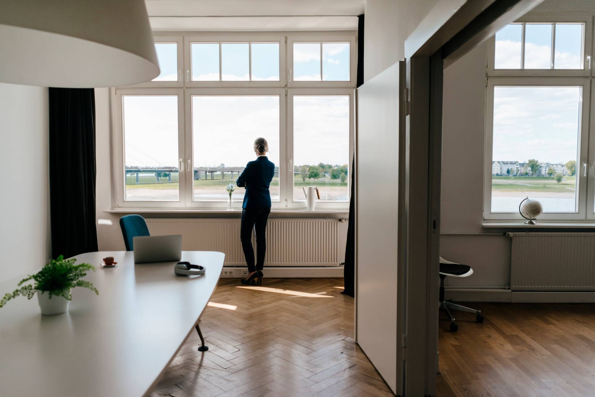 Mujer de negocios de pie en una oficina moderna mirando por la ventana - Puertas y ventanas de pvc Termprotect
