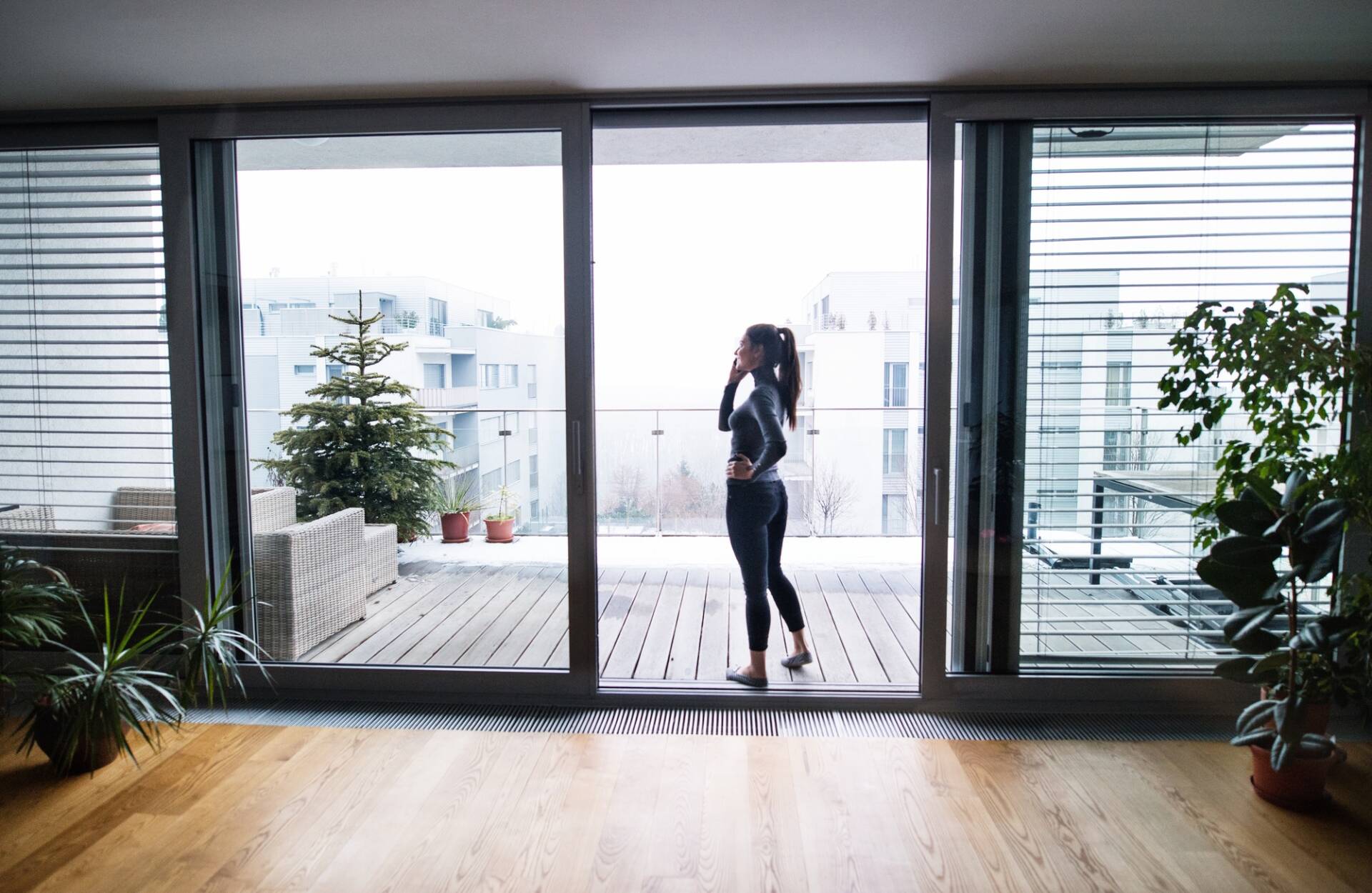 Mujer junto a la ventana con teléfono inteligente, haciendo una llamada telefónica - Puertas y ventanas de pvc Termprotect