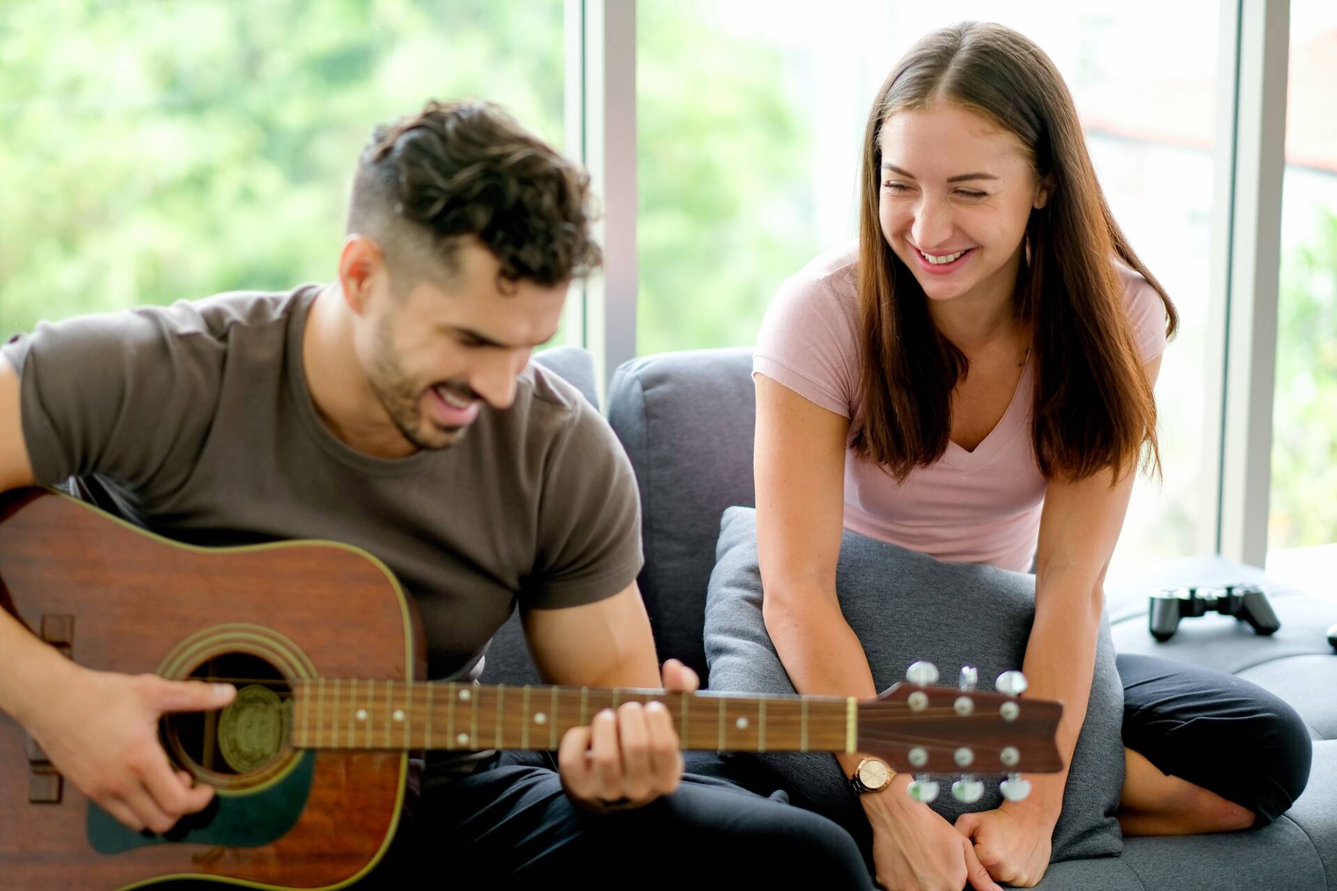 Una mujer disfruta con un hombre tocando la guitarra a su lado en la sala de estar cerca de una ventana de vidrio - Puertas y ventanas de pvc Termprotect