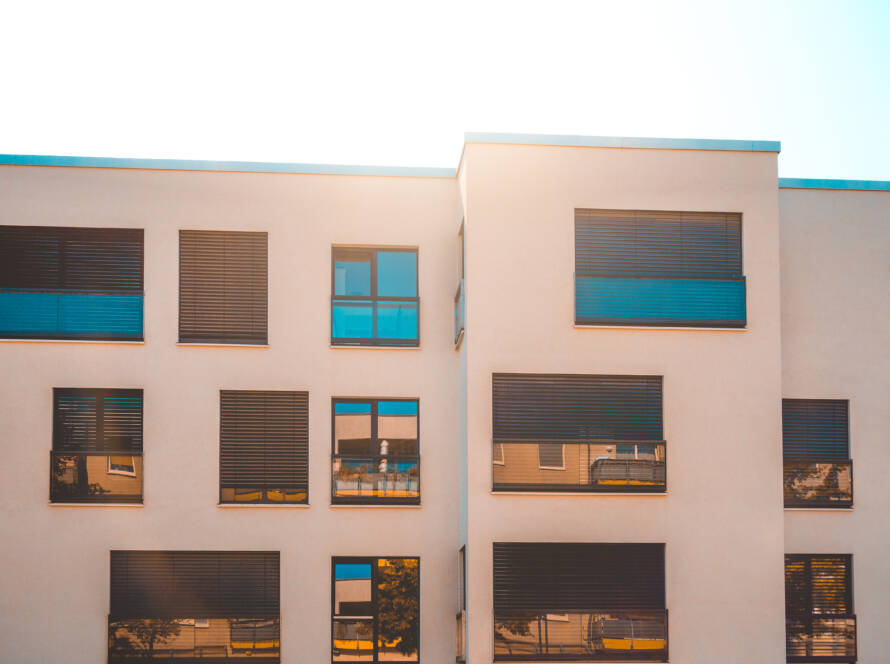 Exterior de edificio moderno con ventanas de PVC de alto rendimiento GEALAN y persianas. Muestra la calidad de instalación de TermProtect y la garantía de 10 años.