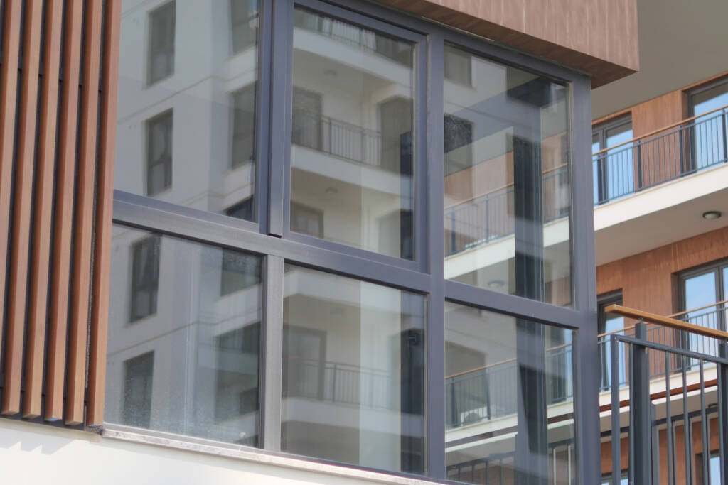 Ventanas de PVC gris oscuro de alto rendimiento en fachada de edificio moderno, con perfilería GEALAN y doble acristalamiento, reflejando el entorno.