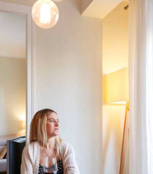 Woman at home, sitting at table, holding glass of wine, looking out of window Mujer en casa, sentada a la mesa, sosteniendo una copa de vino, mirando por la ventana - Puertas y ventanas de pvc Termprotect